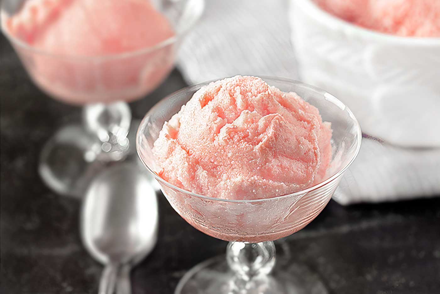 Pink watermelon sorbet served in a clear dessert dish with additional servings in the background.