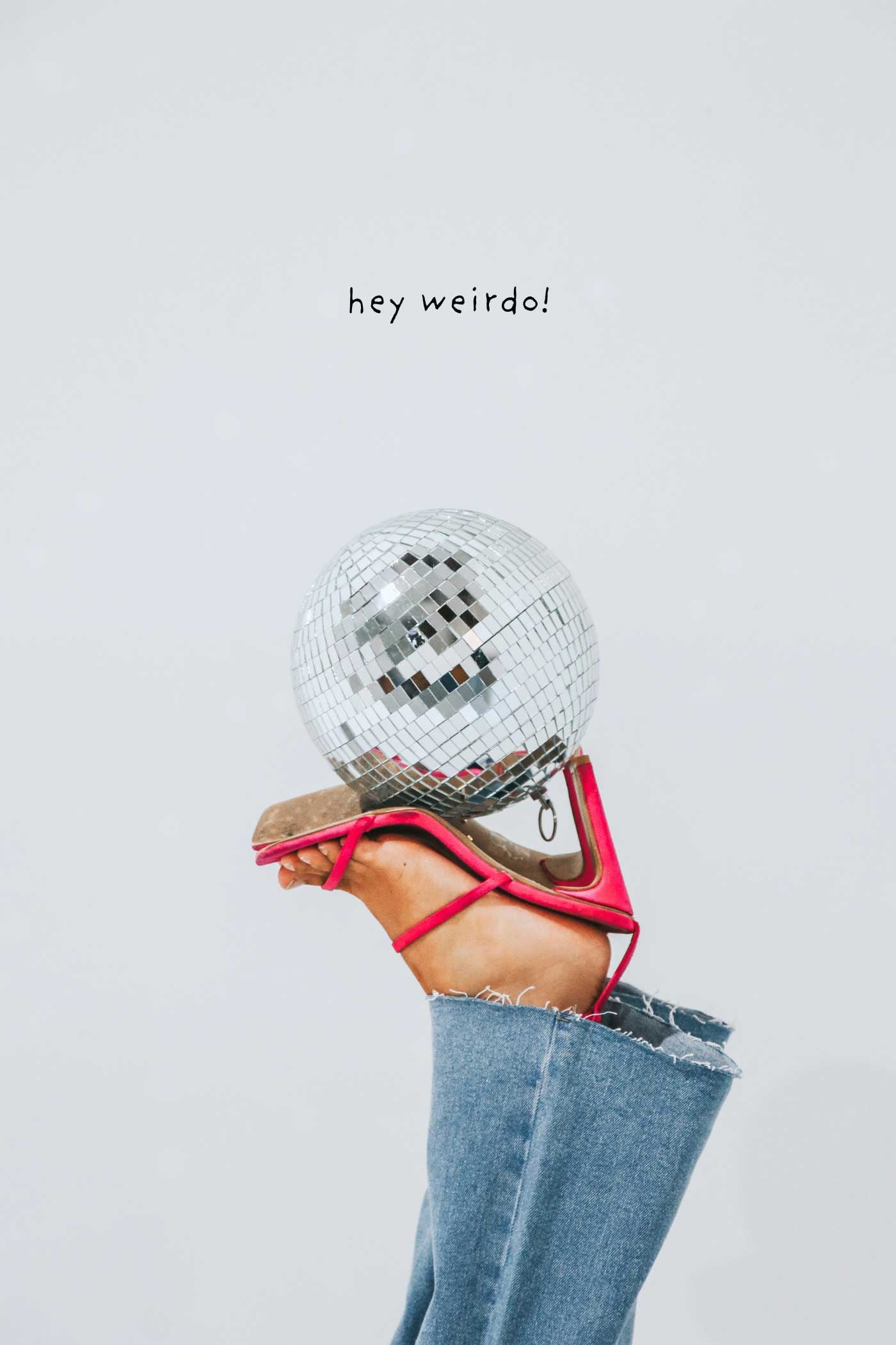 Hand holding a small disco ball beneath the words “hey weirdo”