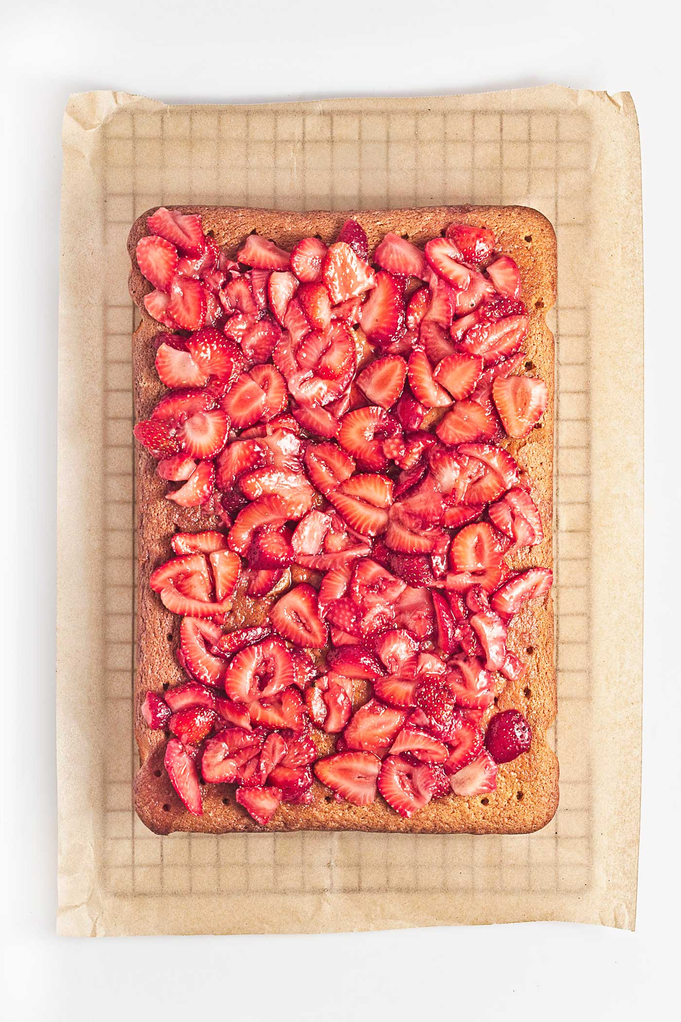 Macerated strawberries spread over a poked vanilla sheet cake so the juices can soak into the cake