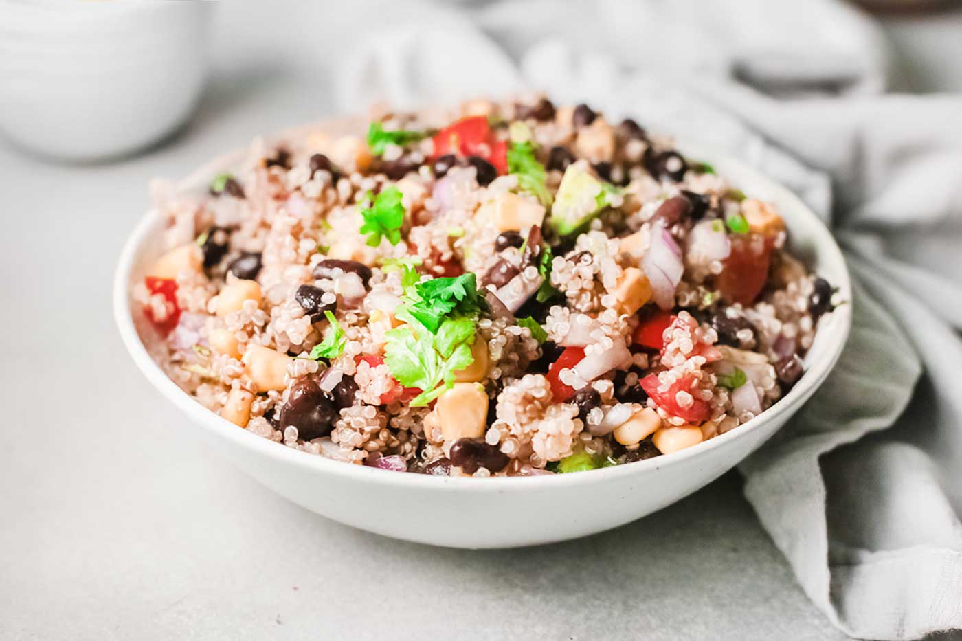 Mexican quinoa salad with black beans, corn, tomatoes, red onion, avocado, and fresh cilantro in a white bowl.