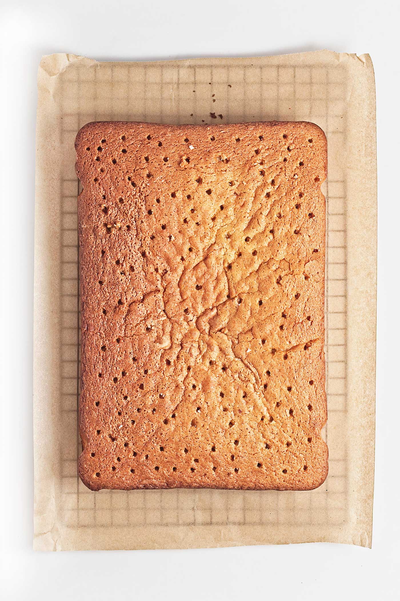 Baked vanilla sheet cake with holes poked across the top before adding macerated strawberries