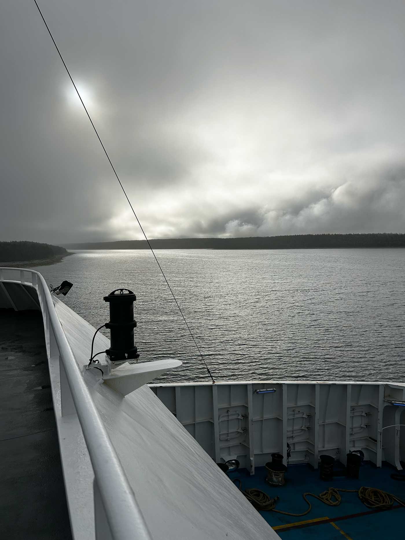 View from the St. Barbe to Blanc-Sablon ferry with dark clouds over calm water and a distant tree-lined shoreline.