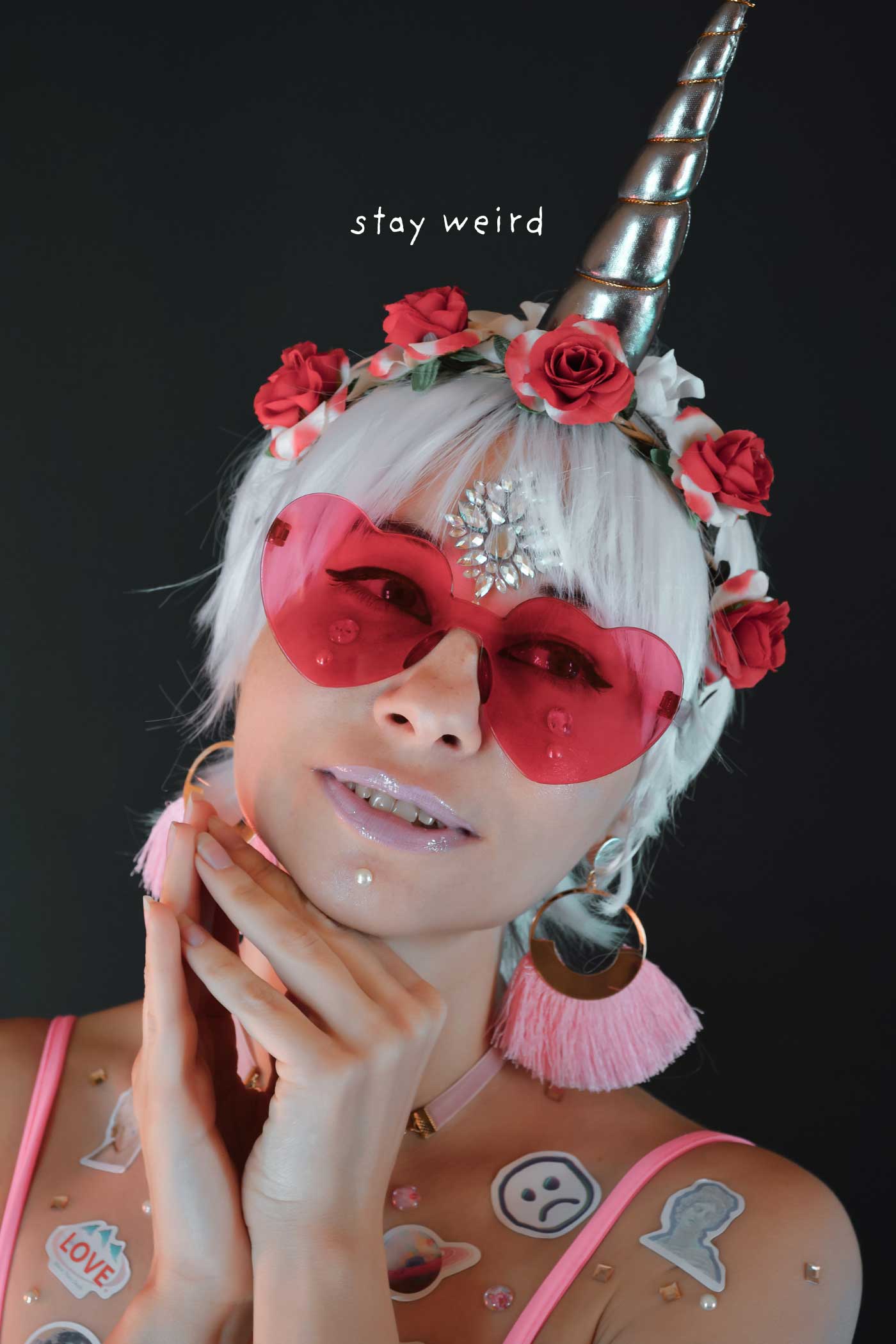 Woman wearing heart-shaped sunglasses, a unicorn horn, and colorful accessories