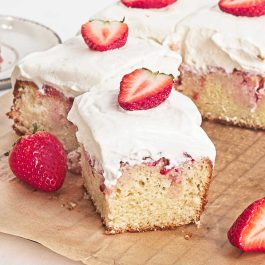 Slice of strawberry shortcake sheet cake with whipped cream, fresh berries, and strawberry filling
