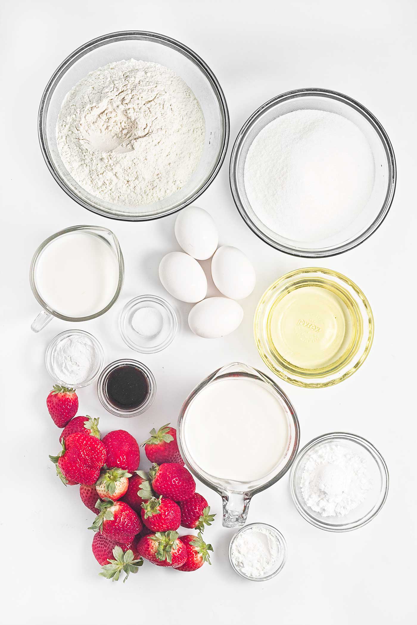 Ingredients for strawberry shortcake sheet cake arranged with fresh strawberries, flour, eggs, milk, oil, sugar, and cream
