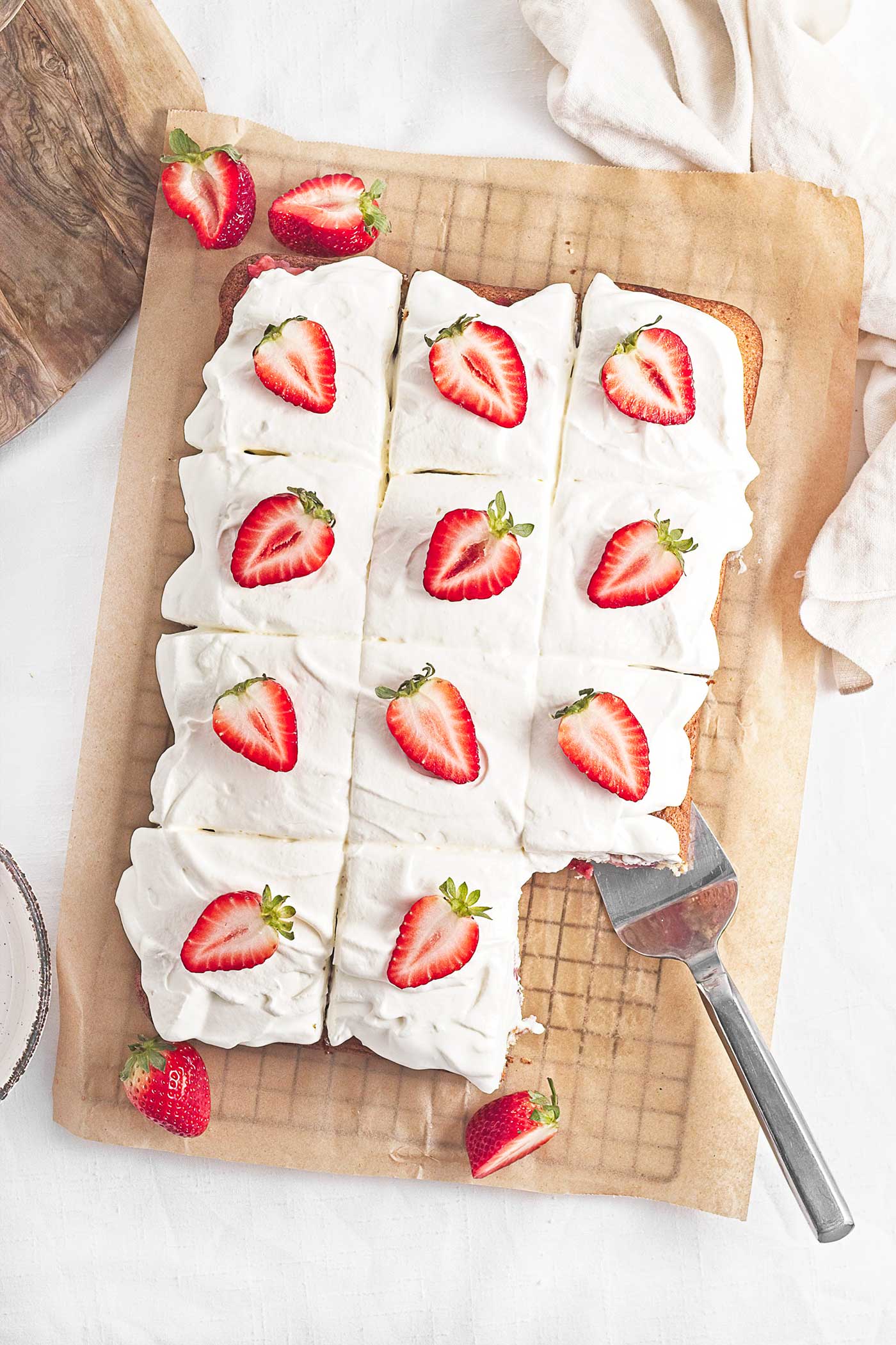 Overhead view of strawberries on whipped topping spread over a sheet cake cut into squares.