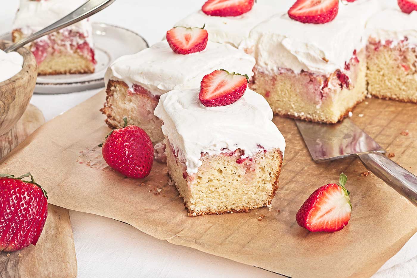 Several pieces of strawberry shortcake sheet cake with fresh strawberries and whipped cream topping, an easy summer recipe