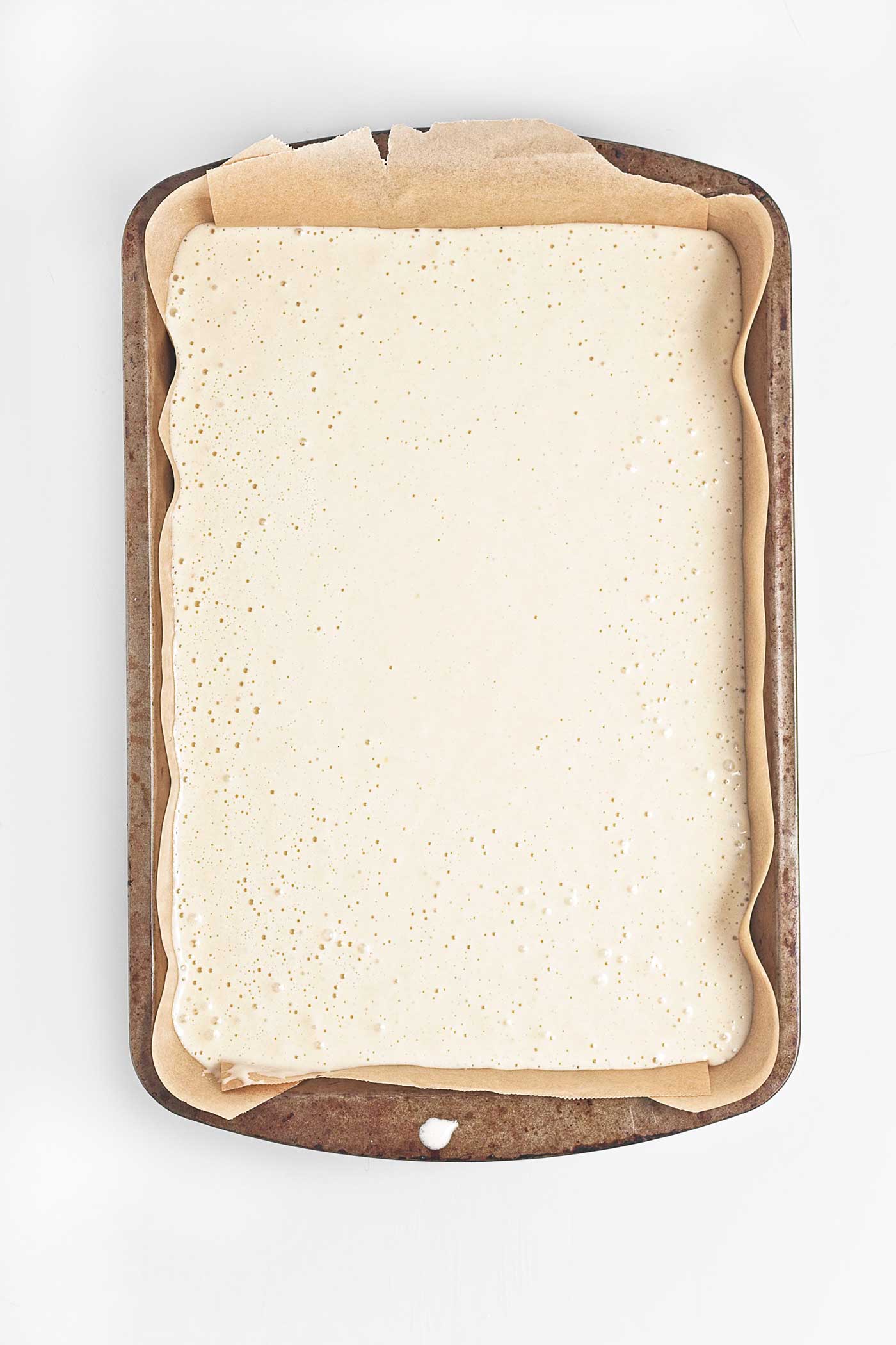 Vanilla cake batter poured into a parchment-lined 9x13 baking pan