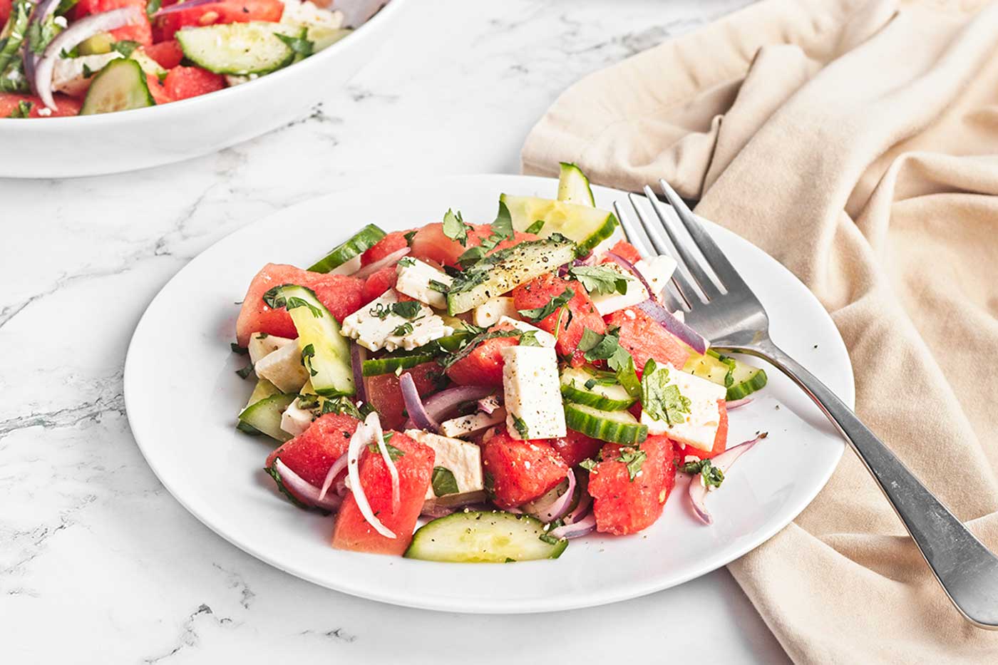 This Watermelon feta salad with cucumber, red onion, fresh herbs, and black pepper served on a white plate is an easy summer recipe.