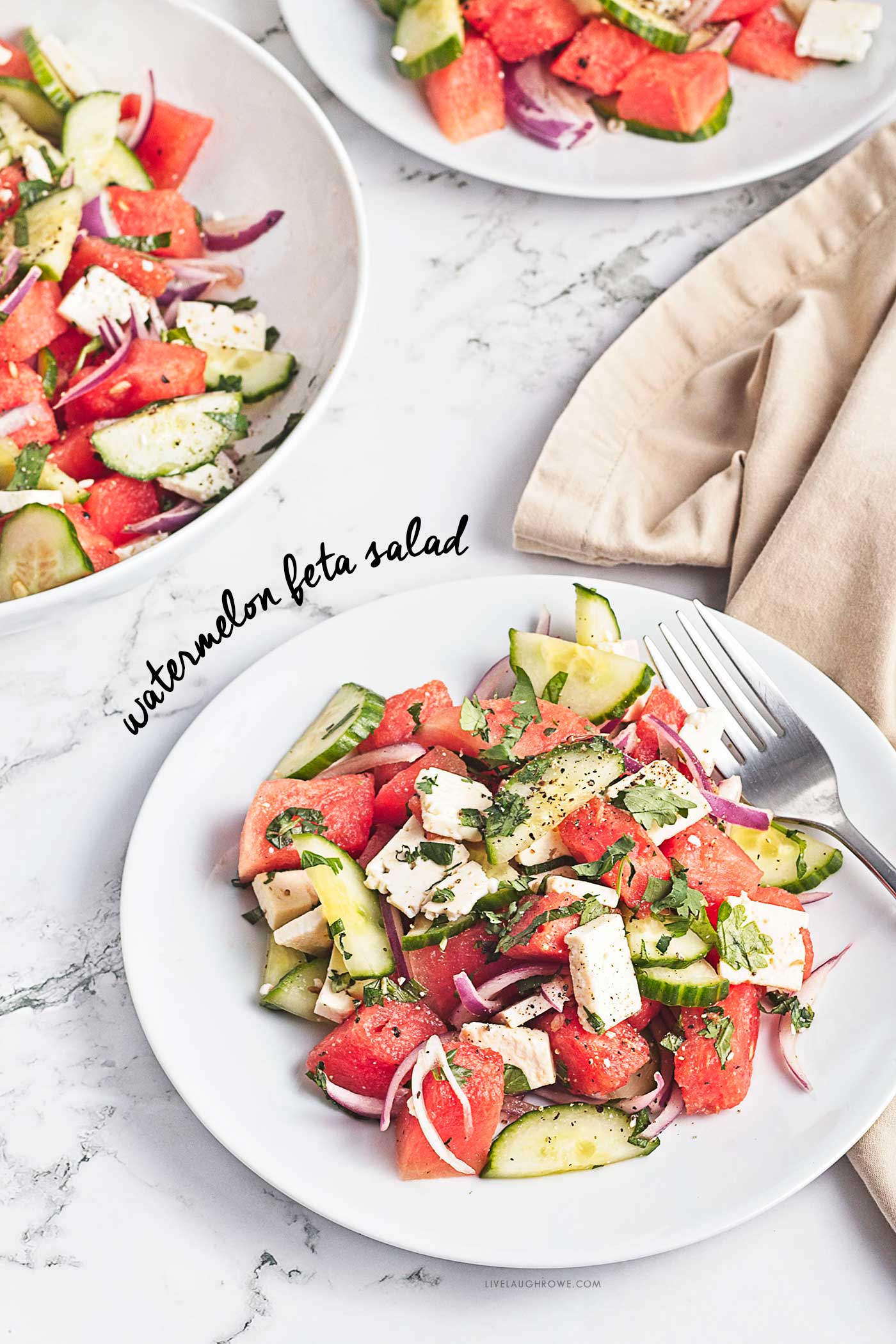 Watermelon feta salad with cucumber, red onion, herbs, lime, and olive oil arranged on a marble surface with text overlay.