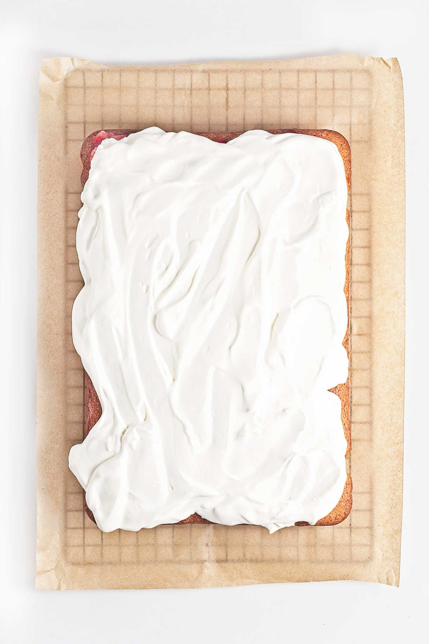Whipped cream spread over strawberries and sheet cake after adding fresh strawberries and juice
