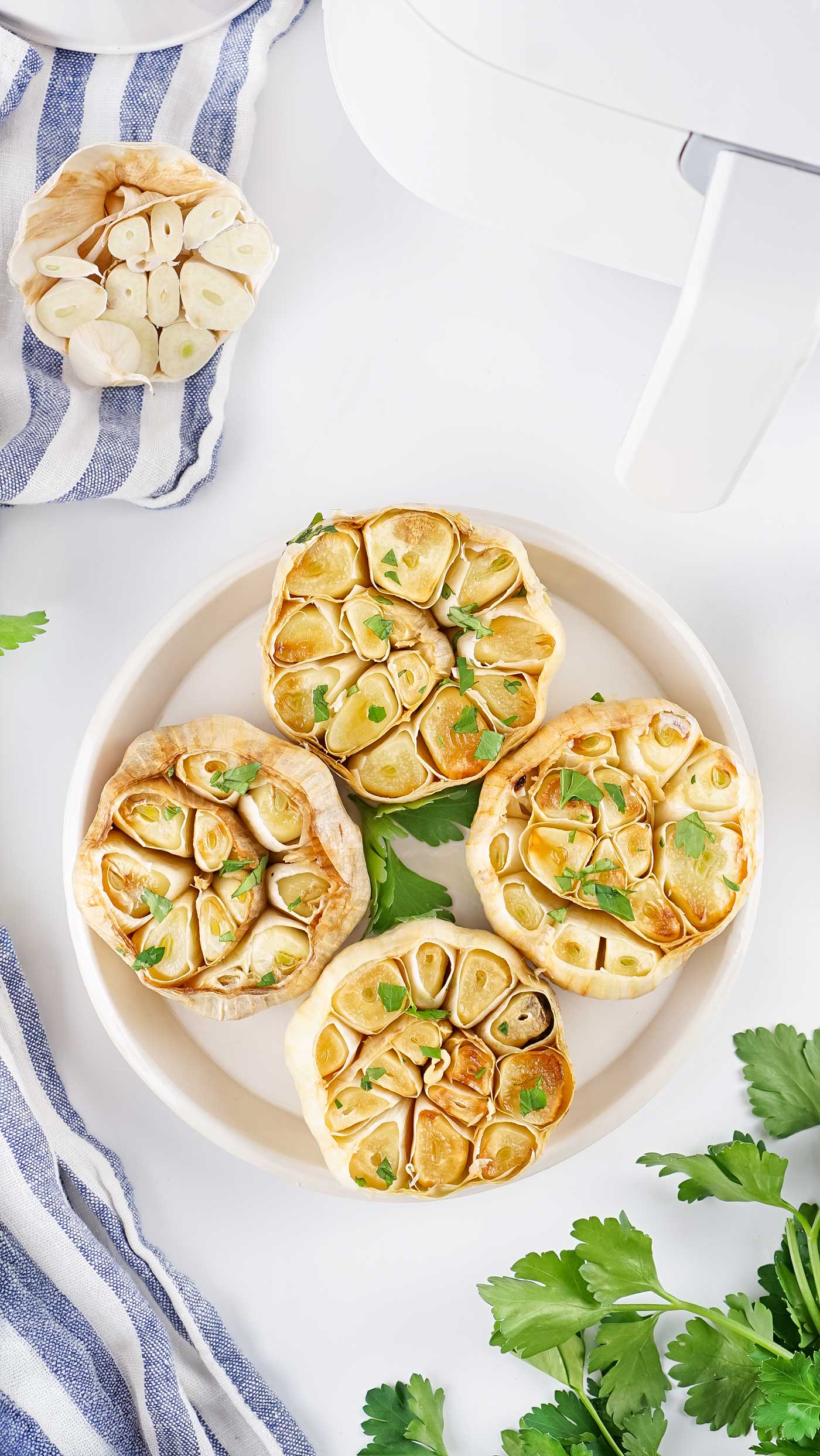 Four golden roasted garlic bulbs on a plate with parsley after cooking in the air fryer.