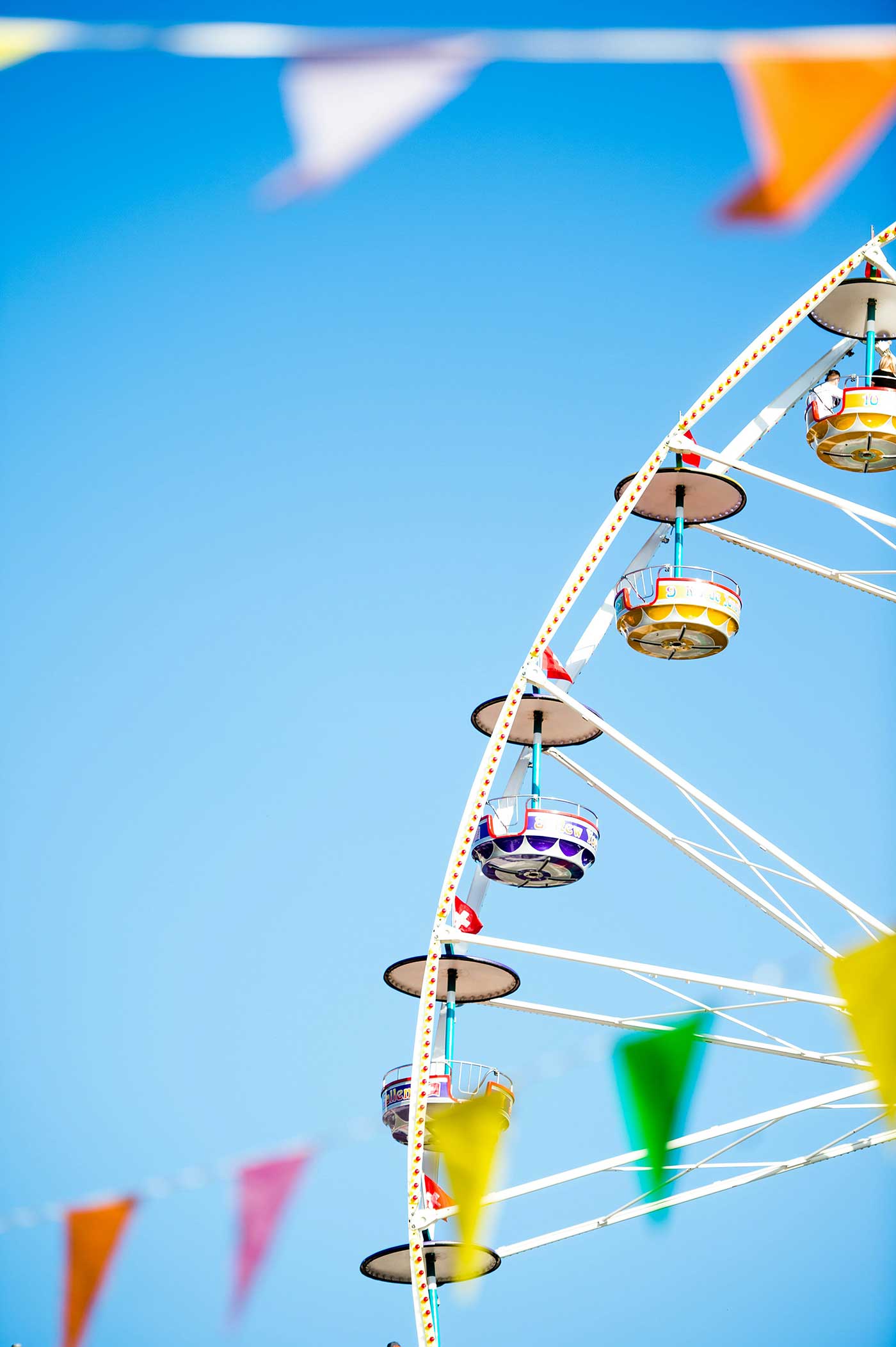Colorful Ferris wheel with flags against a bright blue summer sky.