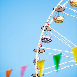 Colorful Ferris wheel with bright carnival flags against a clear blue summer sky.