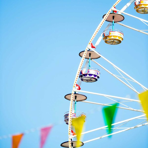 Colorful Ferris wheel with bright carnival flags against a clear blue summer sky.
