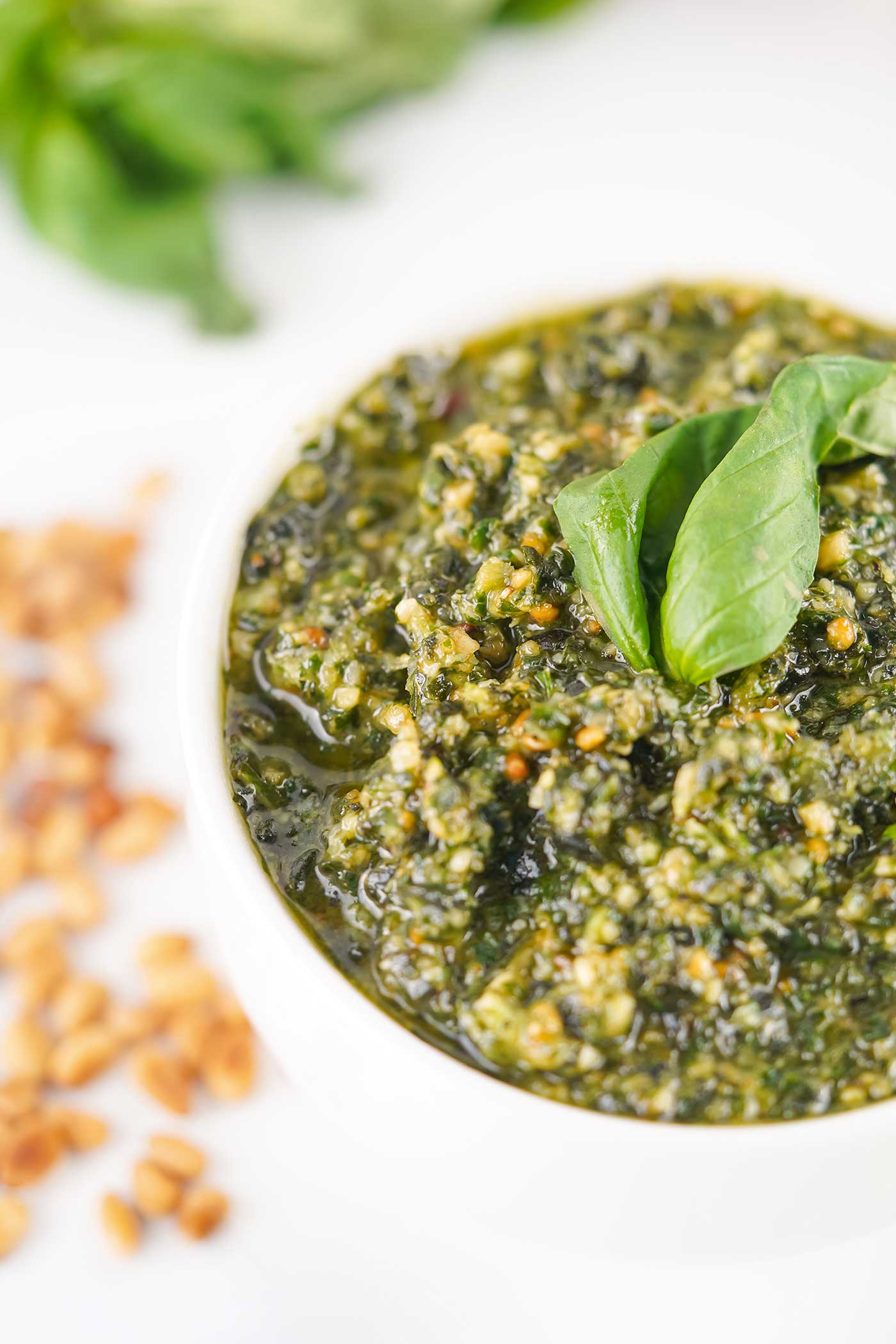 Close-up of homemade basil pesto in a small white bowl topped with fresh basil leaves.