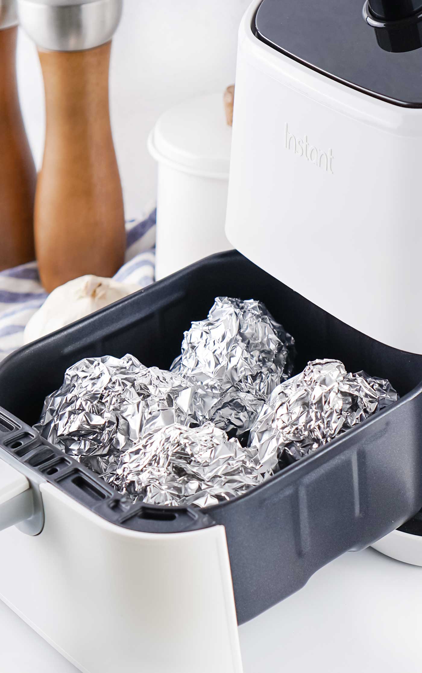 Foil-wrapped garlic bulbs arranged inside an open air fryer basket before cooking.