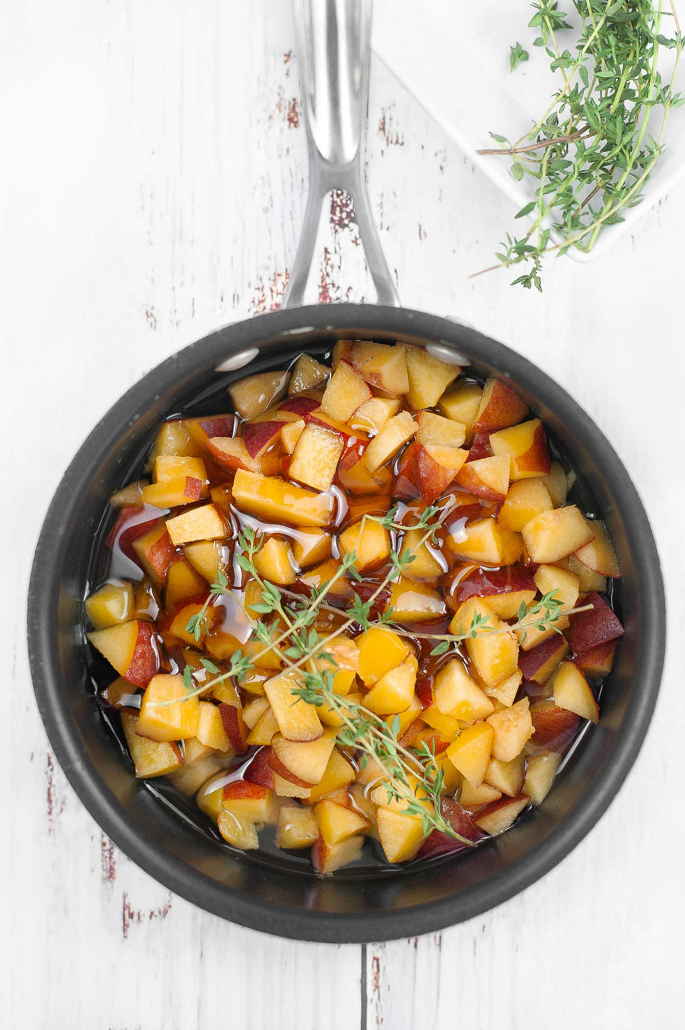 Diced fresh peaches and thyme simmering in a saucepan to make homemade peach syrup.