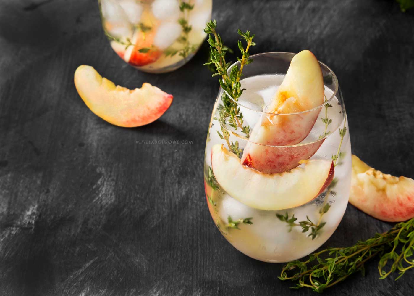 Summer peach cocktail with thyme, ice, and fresh peach slices.