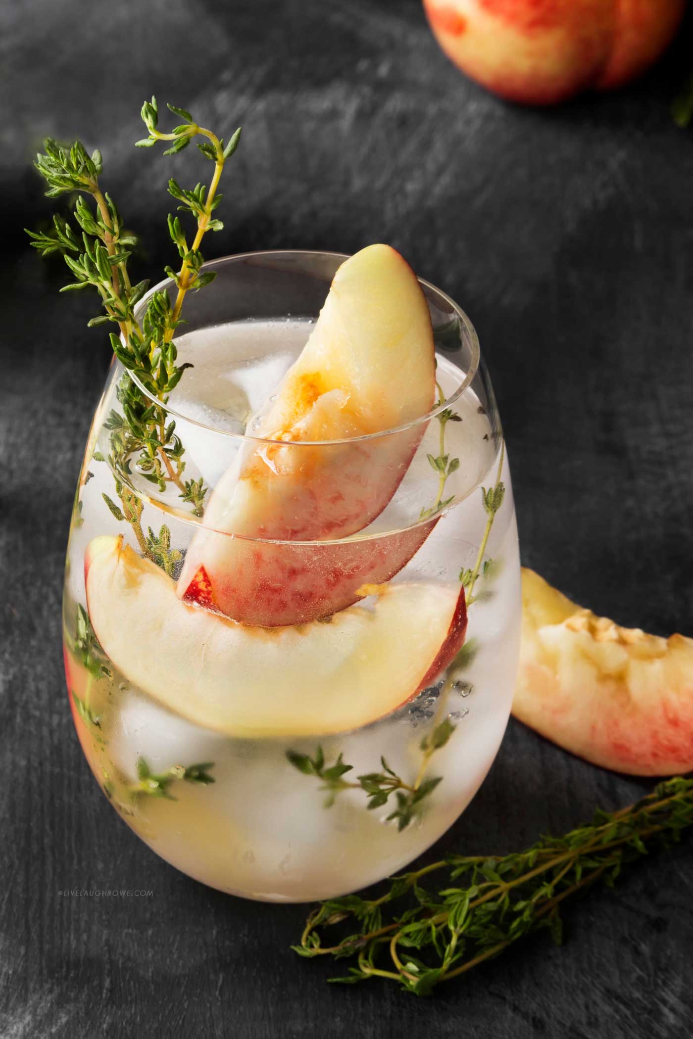 Peach and thyme spritzer garnished with fresh peach wedges and thyme.