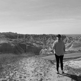 Person standing quietly and looking out over the Badlands in a black-and-white landscape.