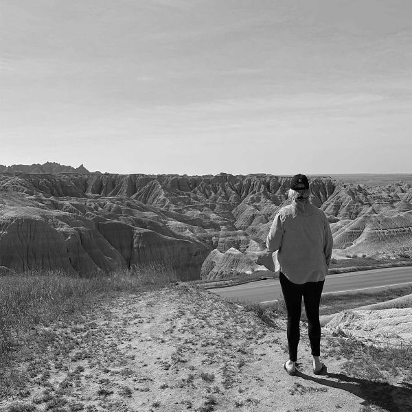 Person standing quietly and looking out over the Badlands in a black-and-white landscape.