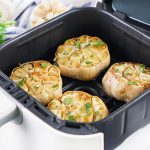 Four golden roasted garlic bulbs topped with parsley inside an open air fryer basket.