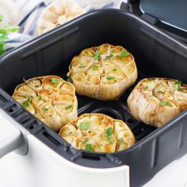 Four golden roasted garlic bulbs topped with parsley inside an open air fryer basket.