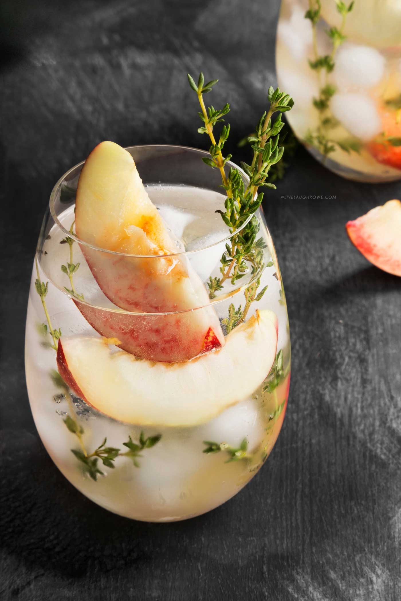 Summer peach cocktail over ice with fresh peach slices and thyme sprigs.