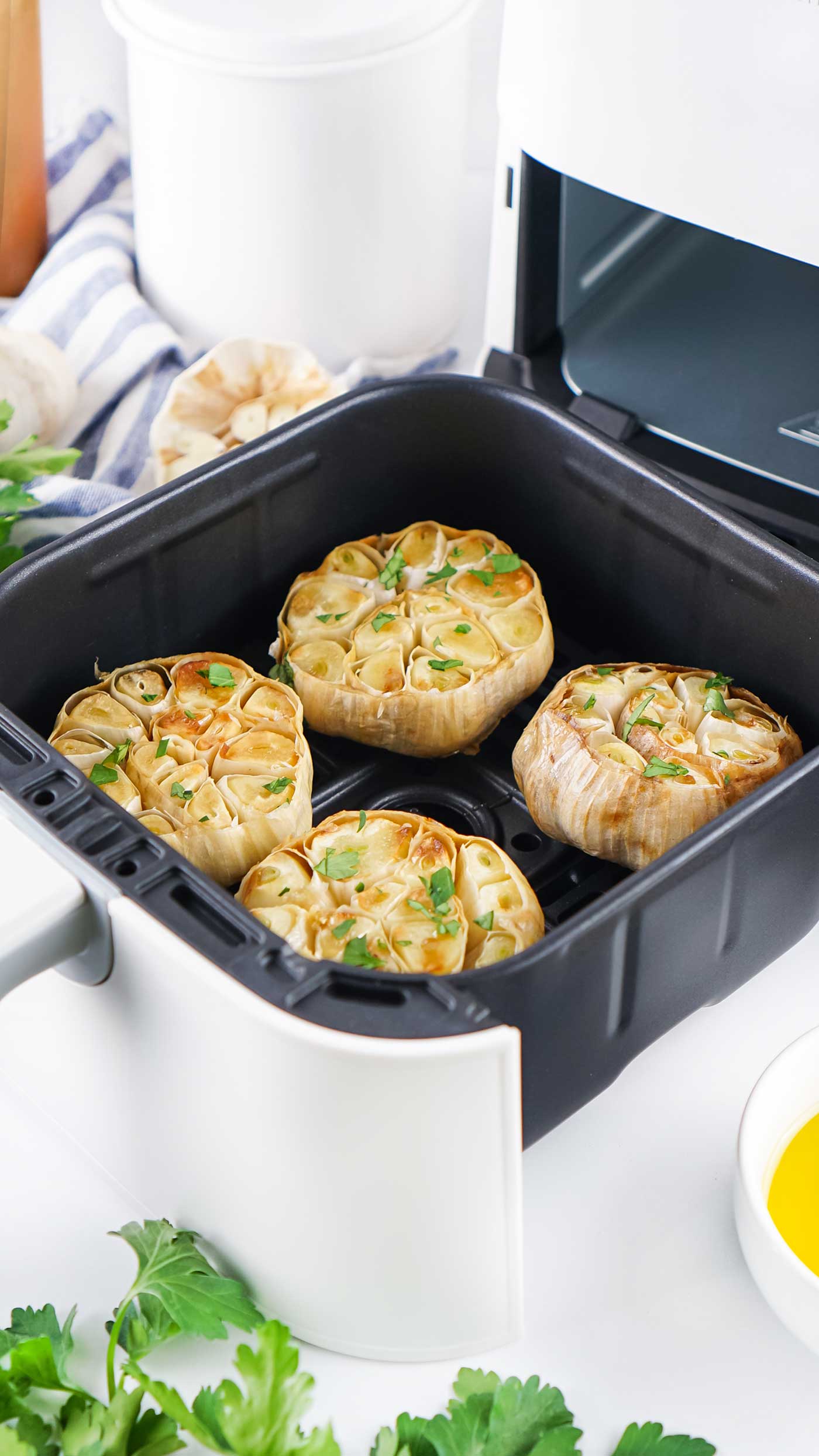Four roasted garlic bulbs inside an open air fryer basket topped with fresh parsley.