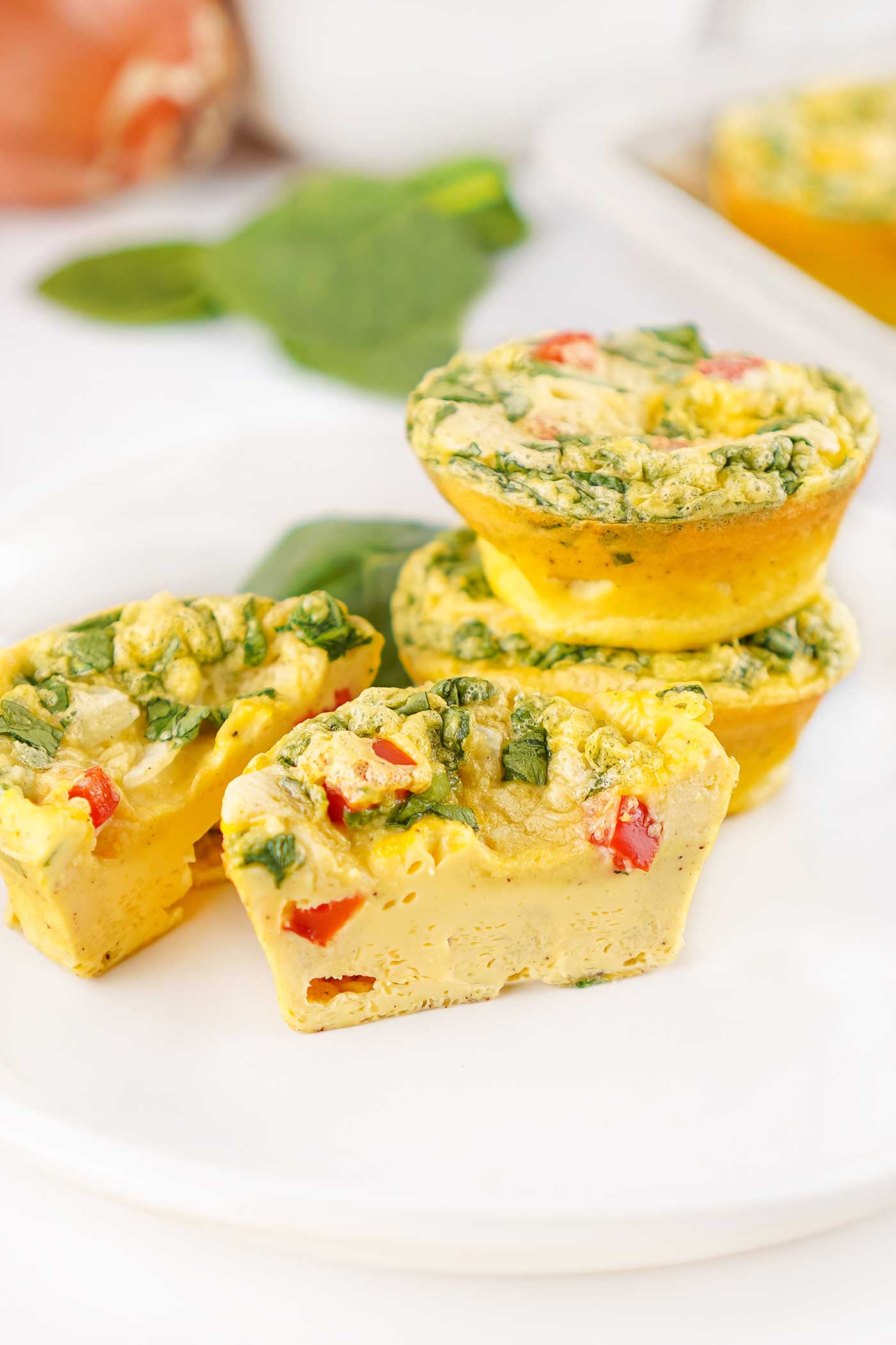 Sliced cottage cheese egg bites with spinach and red bell pepper on a white plate