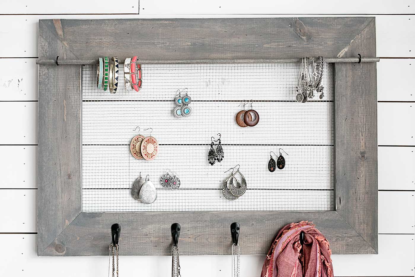 Rustic wood jewelry organizer with wire mesh, hooks, necklaces, bracelets, and accessories