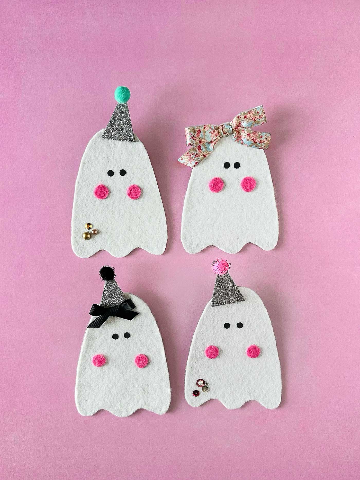 Four DIY felt ghosts decorated with glitter hats, bows, pink cheeks, and small embellishments