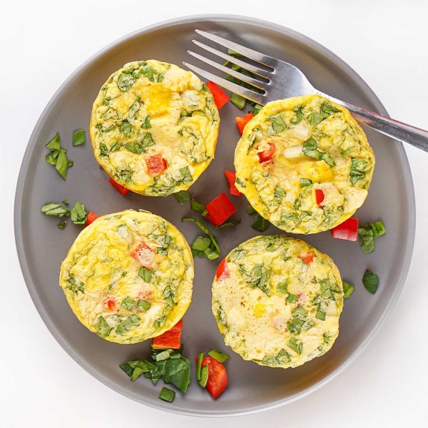 Four egg bites with cottage cheese, spinach, and red bell pepper served on a gray plate