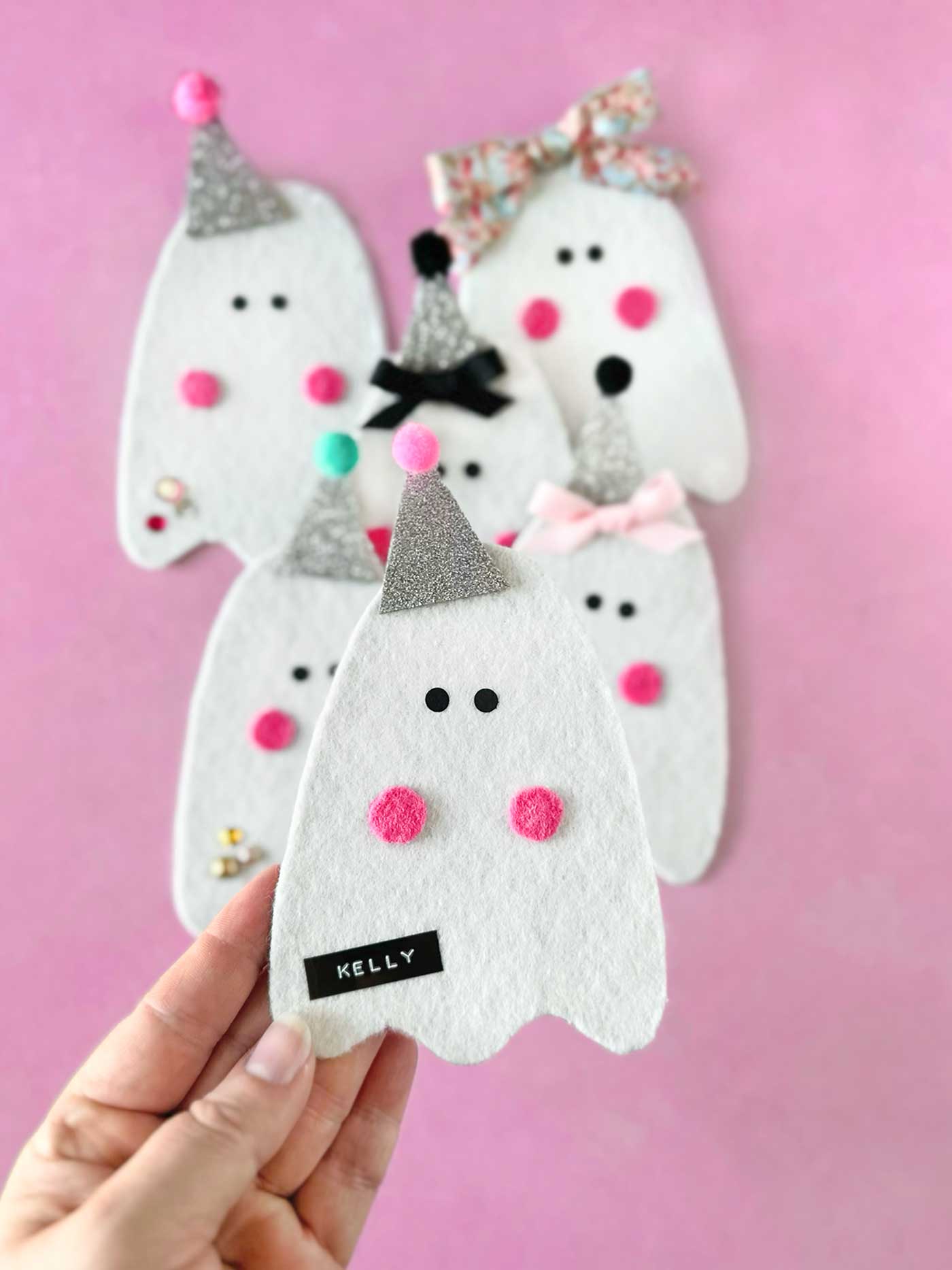 Handmade felt ghost ornament held in hand with black label, glitter hat, and pink felt cheeks
