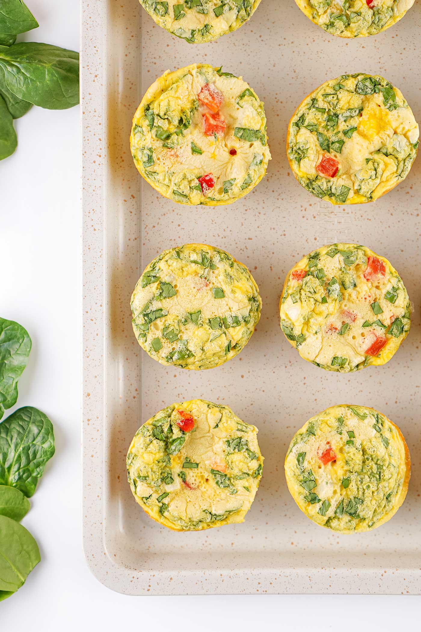 Baked egg bites with spinach and red bell pepper arranged on a rectangular serving platter