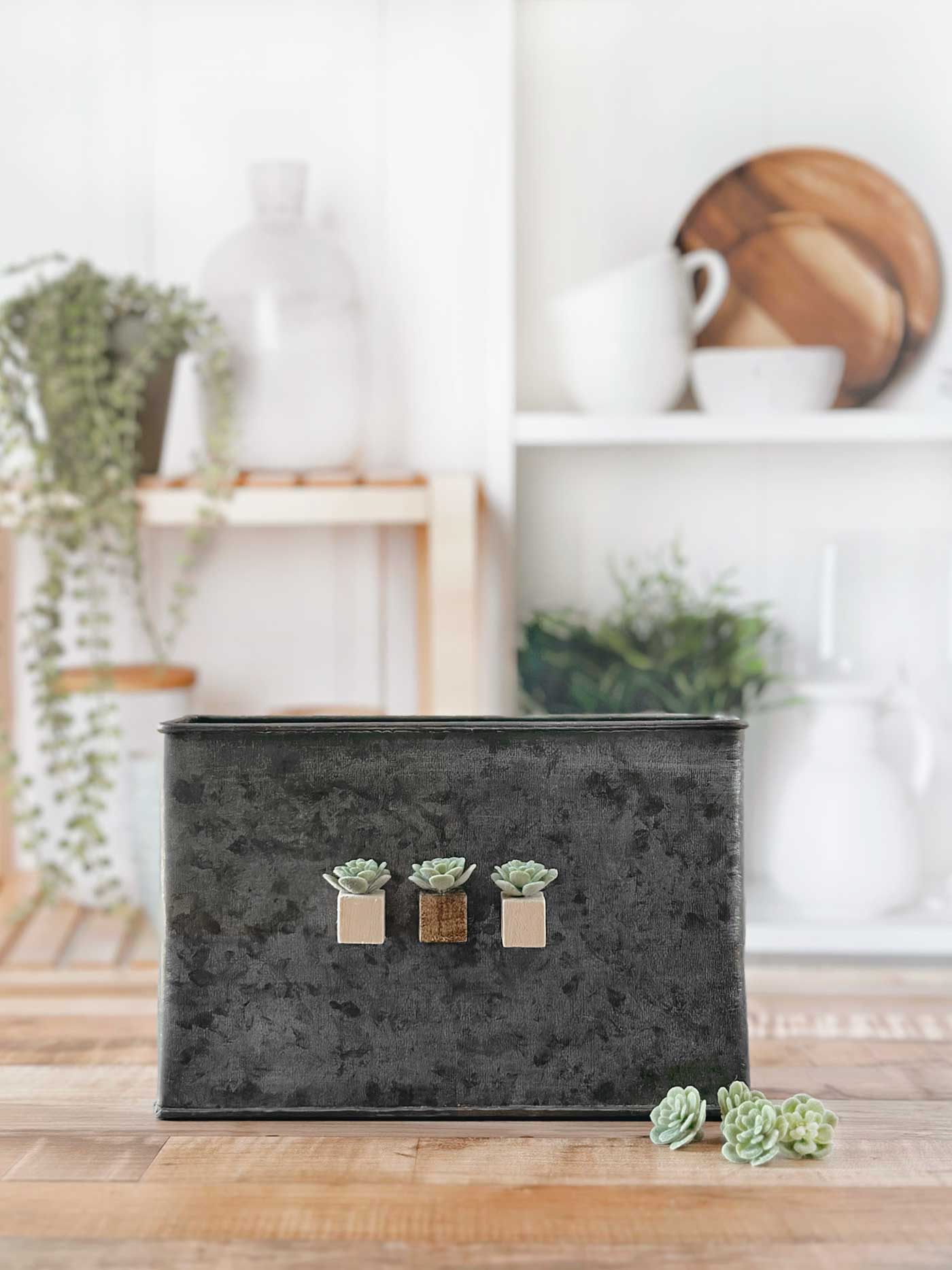 Three faux succulent magnets with natural, brown, and white wood block bases displayed on a dark metal container.