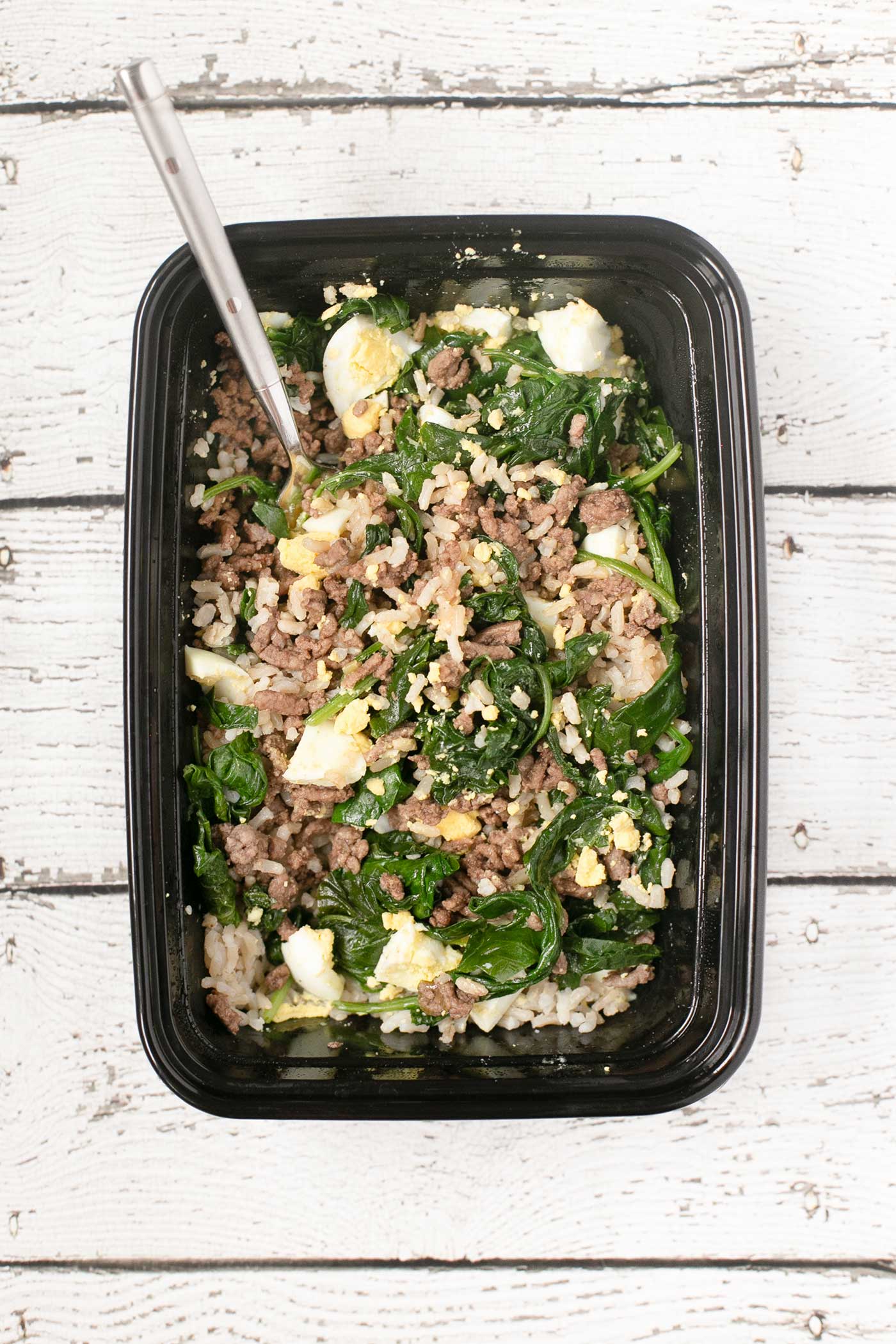 Korean beef bowl meal prep with rice, spinach, seasoned beef, and hard-boiled egg mixed together.