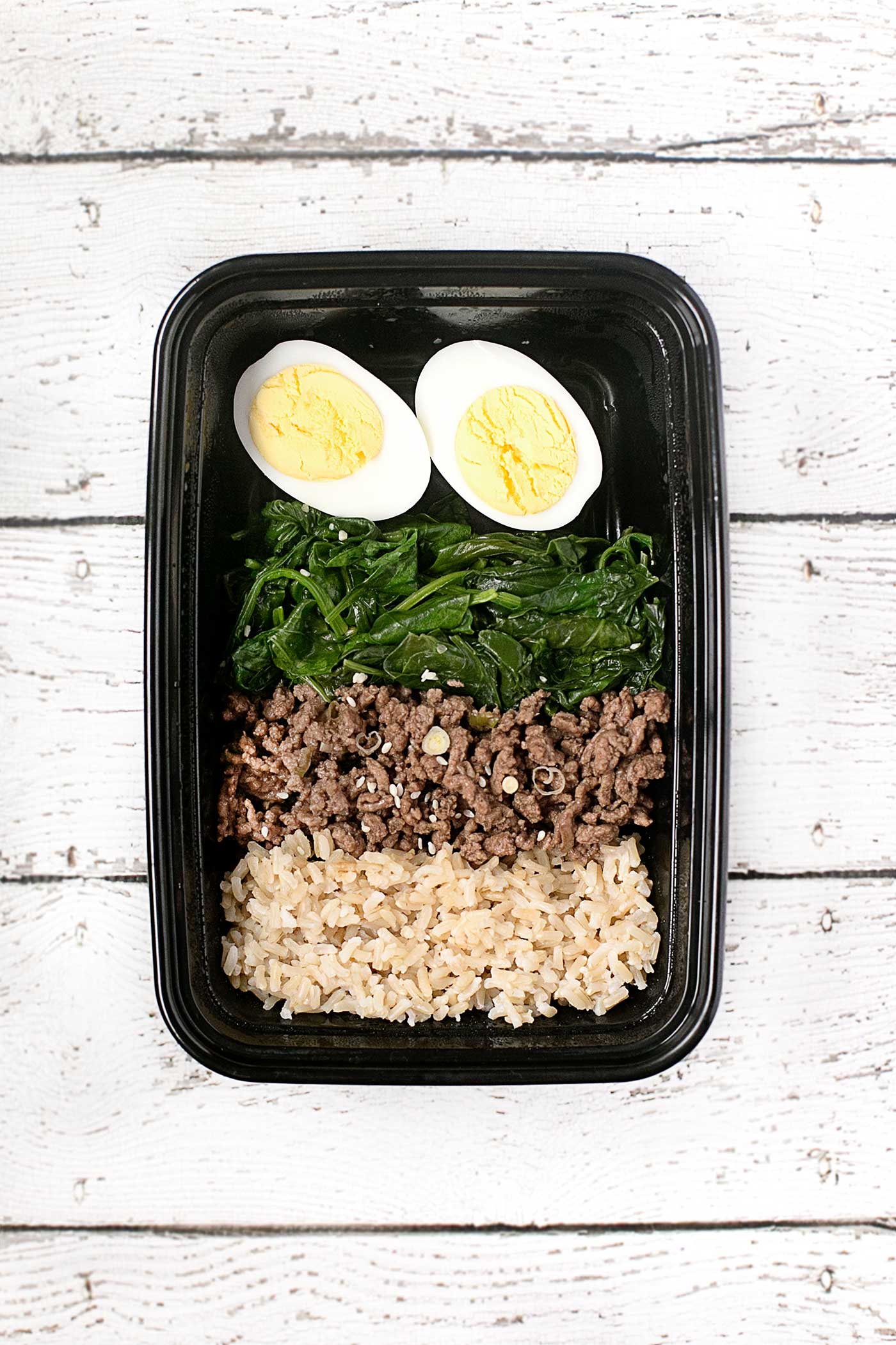 Korean beef meal prep bowl with brown rice, seasoned beef, spinach, and hard-boiled eggs.