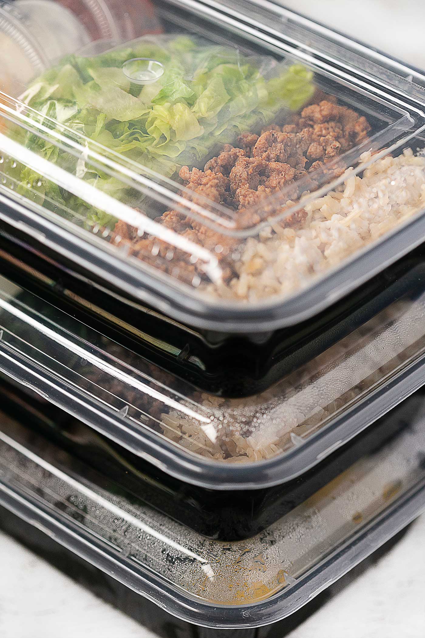 Stacked meal prep containers filled with taco salad ingredients for make-ahead lunches.