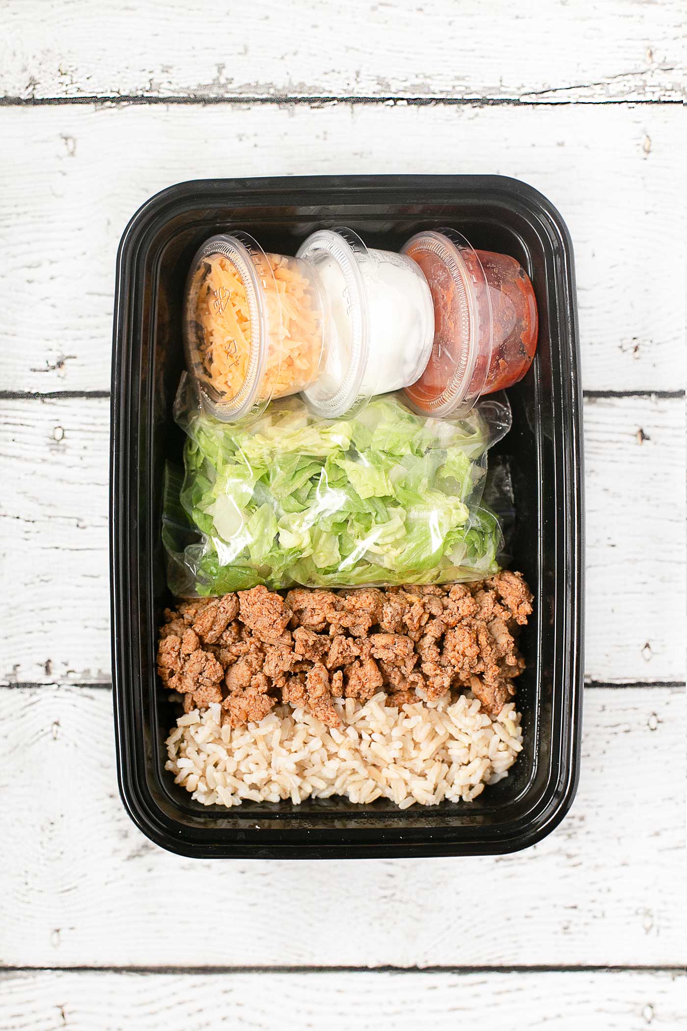Taco salad meal prep bowl with lettuce, seasoned ground meat, rice, and toppings ready for the week.
