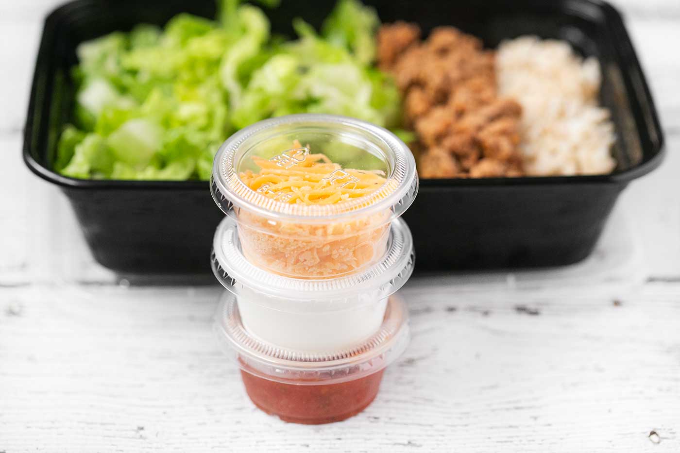 Taco salad meal prep with separate containers of shredded cheddar cheese, sour cream, and salsa.